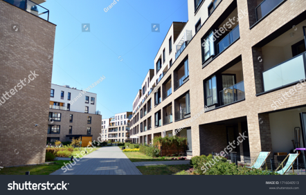 Modern multifamily apartment community with brick buildings, private balconies, landscaped green spaces, and a pedestrian walkway.